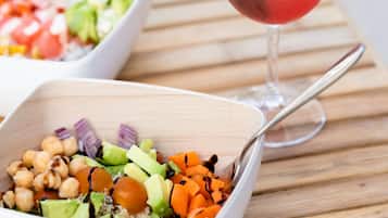 A wooden table with two white bowls containing salads and a glass of red drink with a mint garnish.