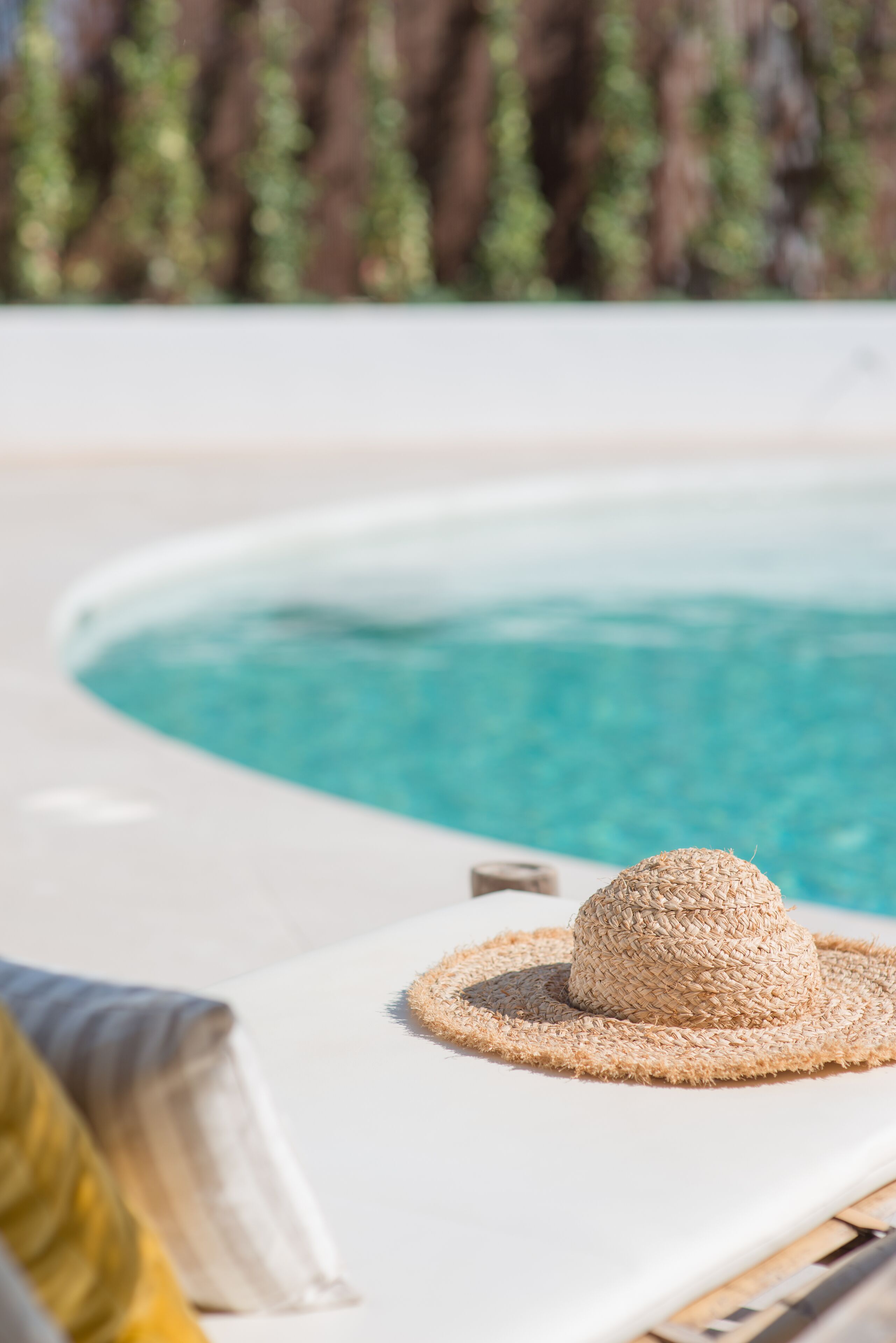 Eine Liege am Pool mit Sonnenhut und Handtuch.