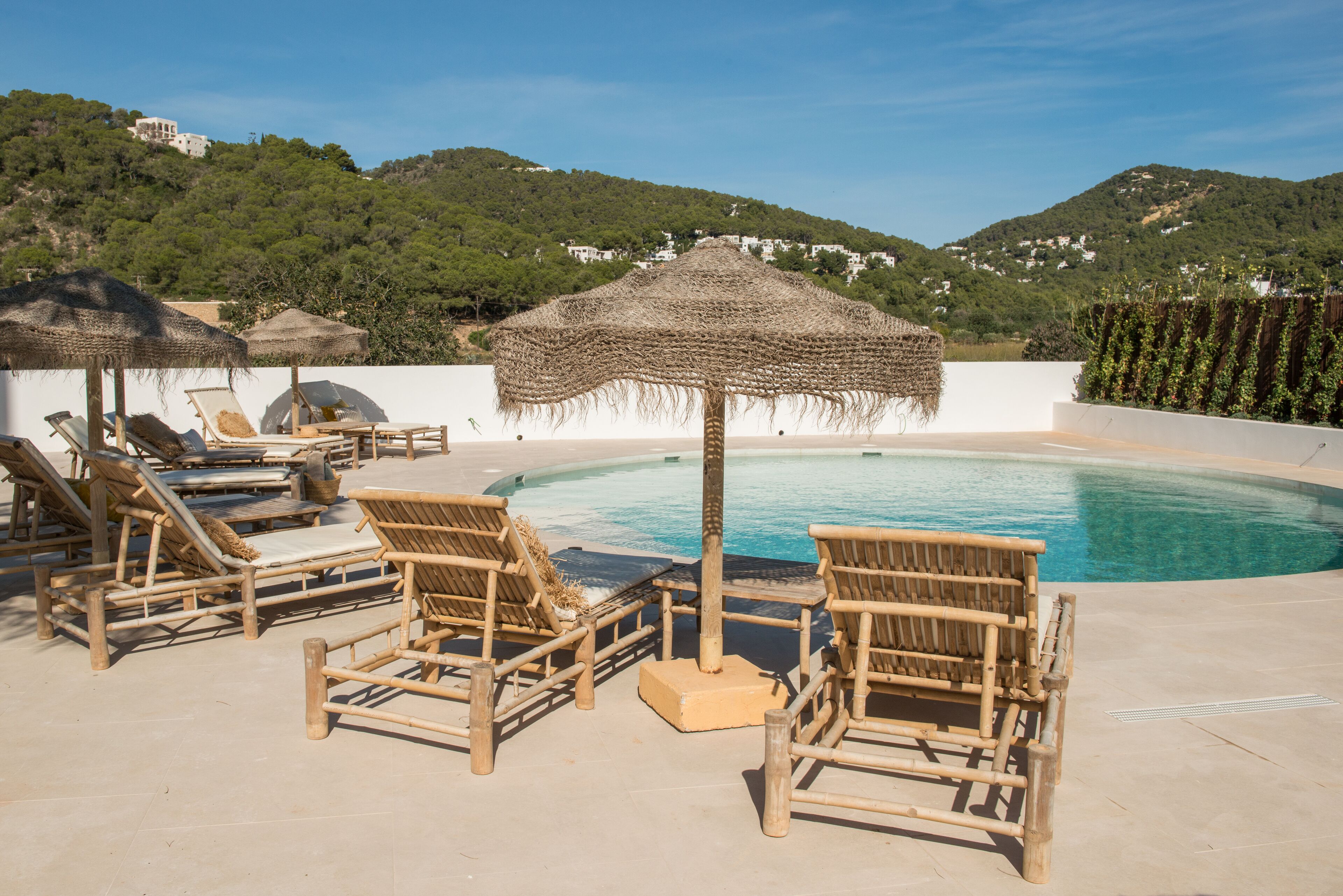 A poolside area with lounge chairs and umbrellas, surrounded by a pool and a view of hills.