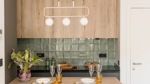 A modern kitchen with wooden cabinets, a green tiled backsplash, and a dining table set with plates, glasses, and a plant. - The Olive Boutique Suites and Spa (Santa Eulalia del Rio)