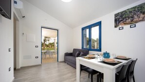 Ein modernes Wohnzimmer mit Essbereich, einem grauen Sofa, einem weißen Tisch und einem Fenster mit blauem Rahmen.