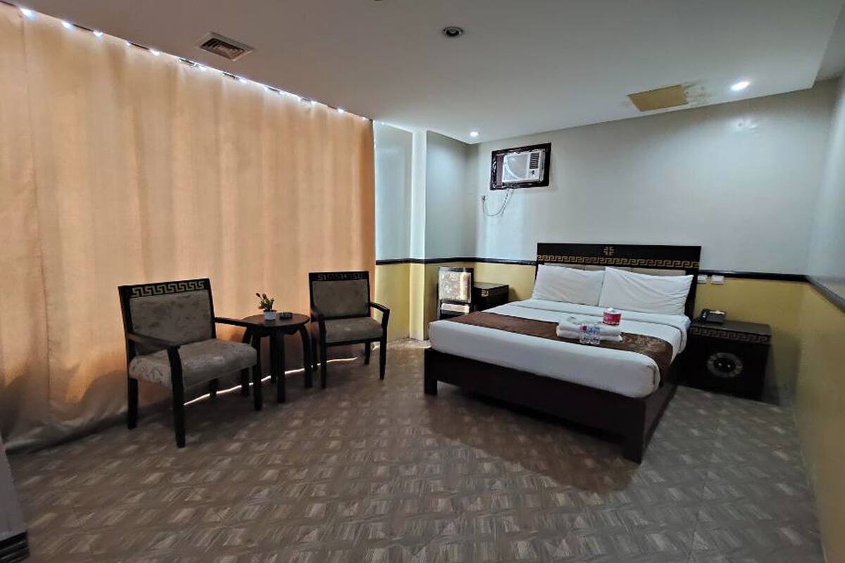 Une chambre d’hôtel avec un lit, deux chaises, une petite table et une table de chevet.