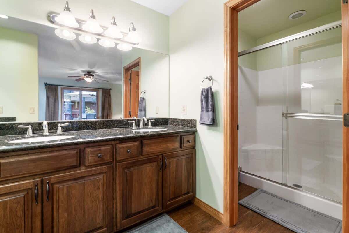 A bathroom with a double sink vanity, a glass shower enclosure, and a ceiling fan.