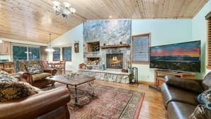 Una sala de estar acogedora con chimenea de piedra, sofás de cuero, un comedor y un televisor grande.