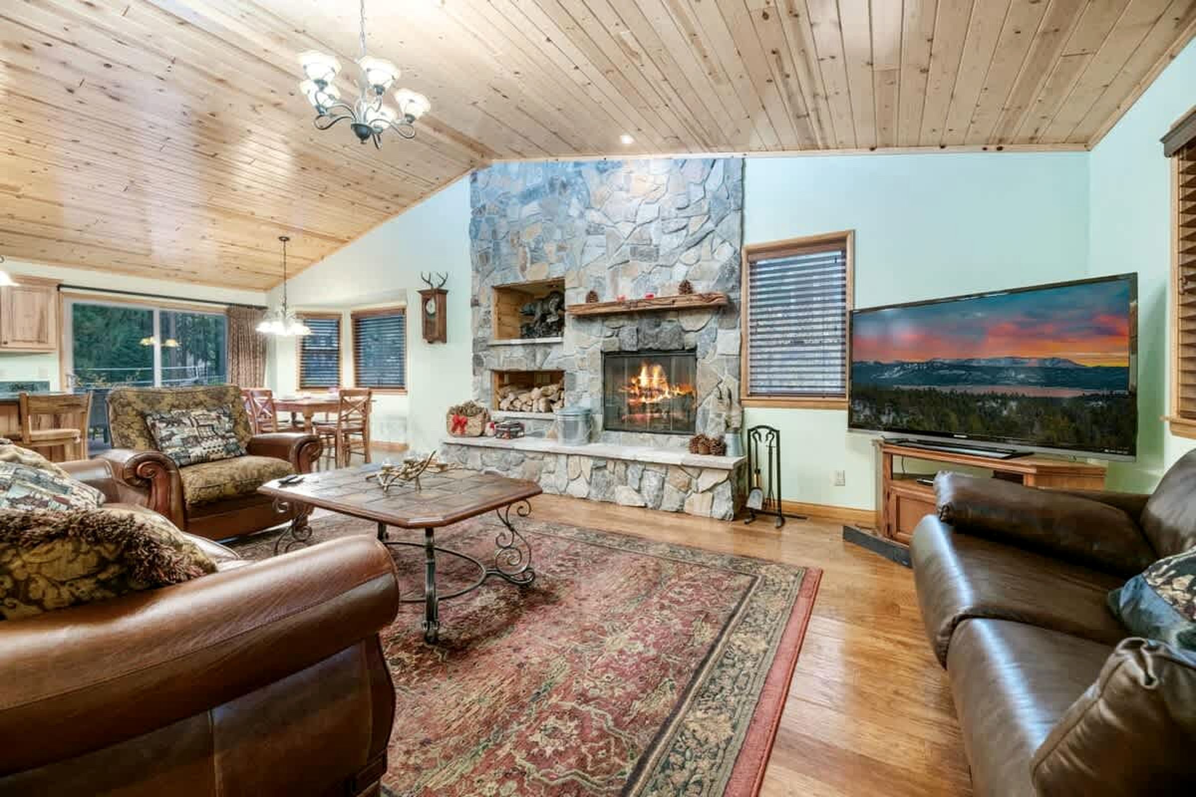 Una sala de estar acogedora con chimenea de piedra, sofás de cuero, una mesa de centro y un televisor grande.