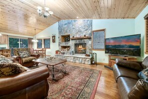 Una sala de estar acogedora con chimenea de piedra, sofás de cuero, una mesa de centro y un televisor grande.