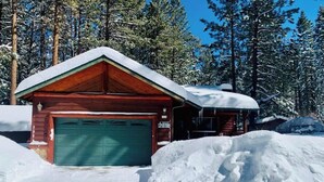 Una cabaña de madera con una puerta de garaje verde, rodeada de nieve y árboles.