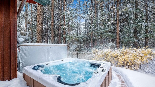 Un jacuzzi rodeado de árboles cubiertos de nieve y una estructura de madera.