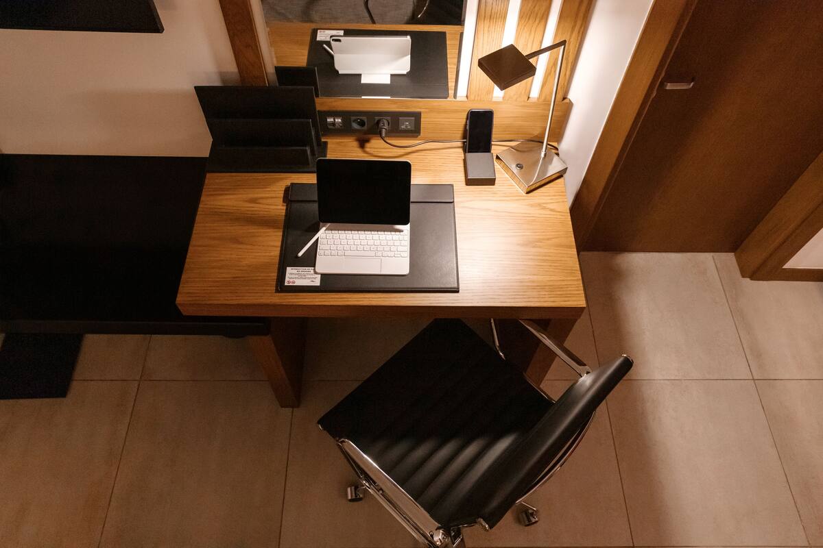 A modern office space with a wooden desk, a laptop, a smartphone, and a black chair.