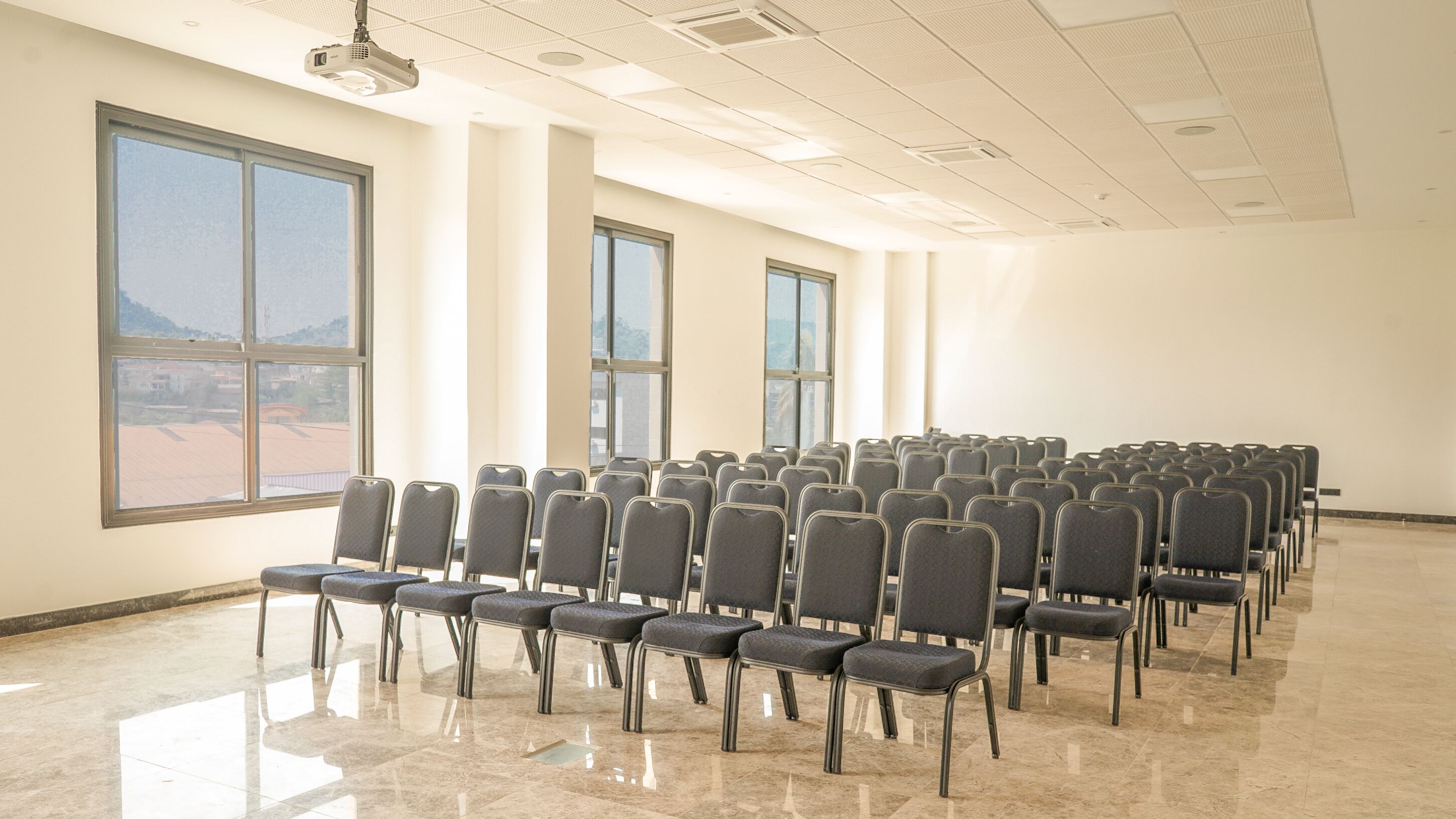 A conference room with rows of chairs, large windows, and a ceiling-mounted projector.