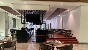 Un restaurante moderno con una barra central, varias mesas de comedor y una escalera que conduce a un nivel superior.