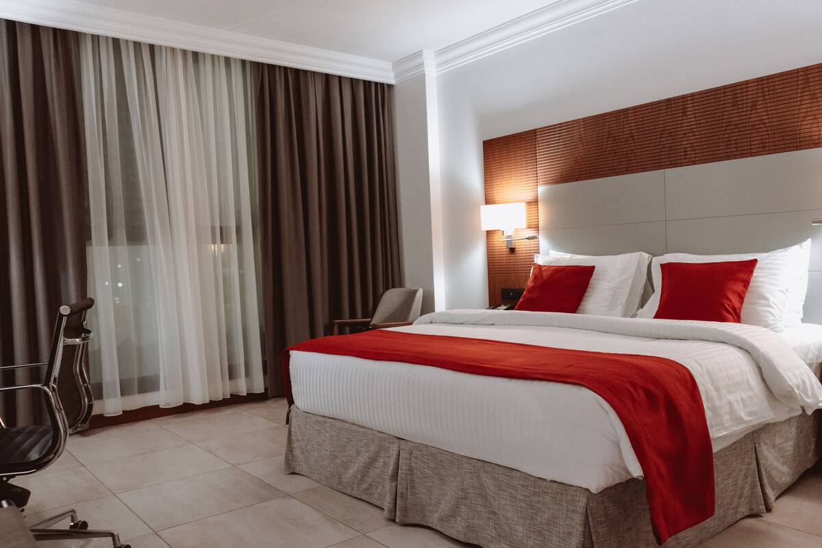 A hotel room with a large bed, a chair, a desk, and a window with curtains.