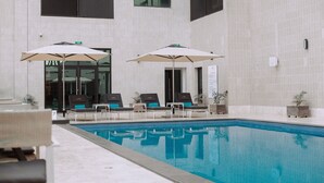 Una piscina con sillas de descanso y sombrillas, rodeada por la fachada de un edificio con azulejos.