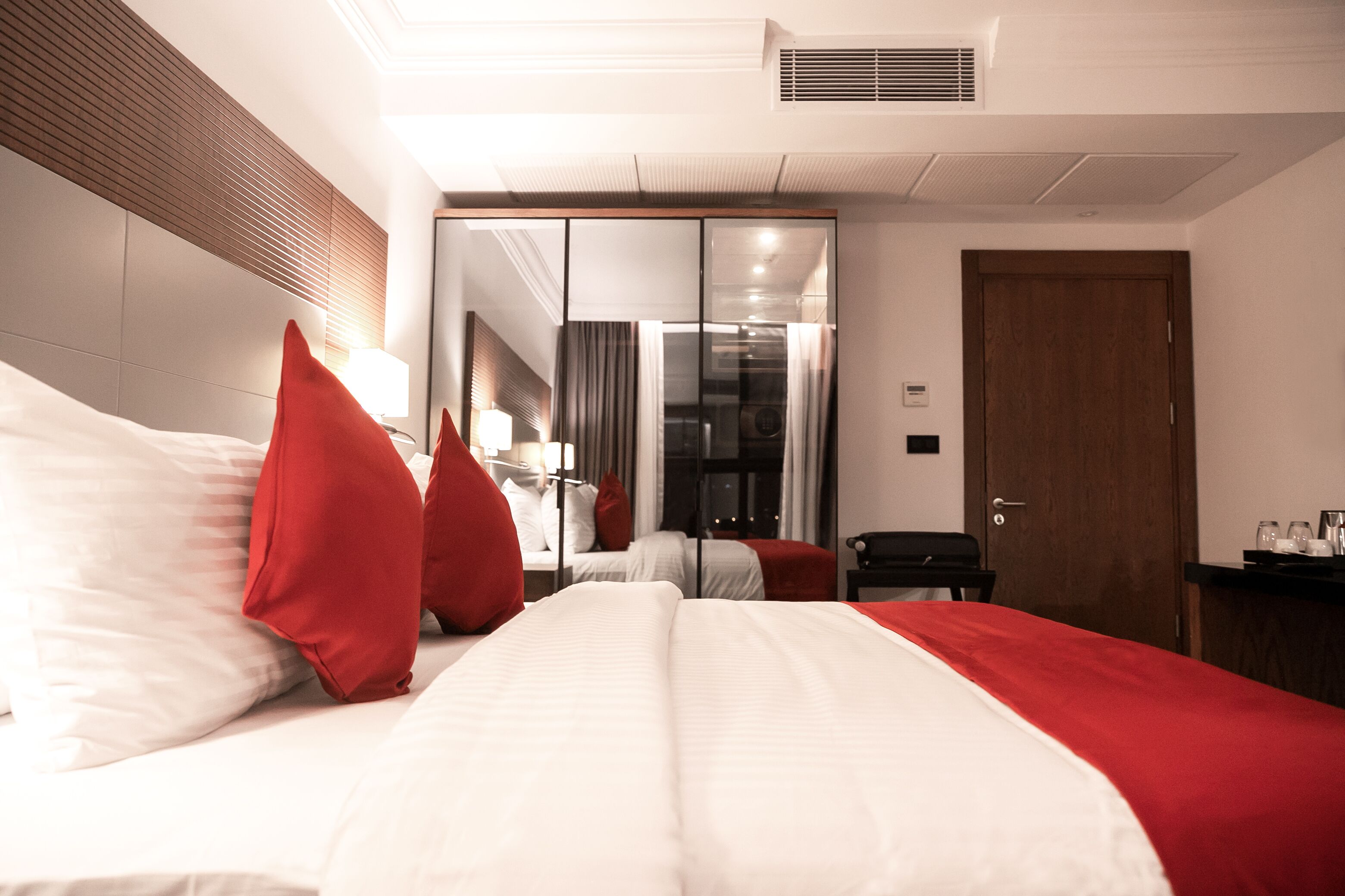 Een hotelkamer met een groot bed, rode en witte beddengoed, een bureau met stoel en een spiegel.