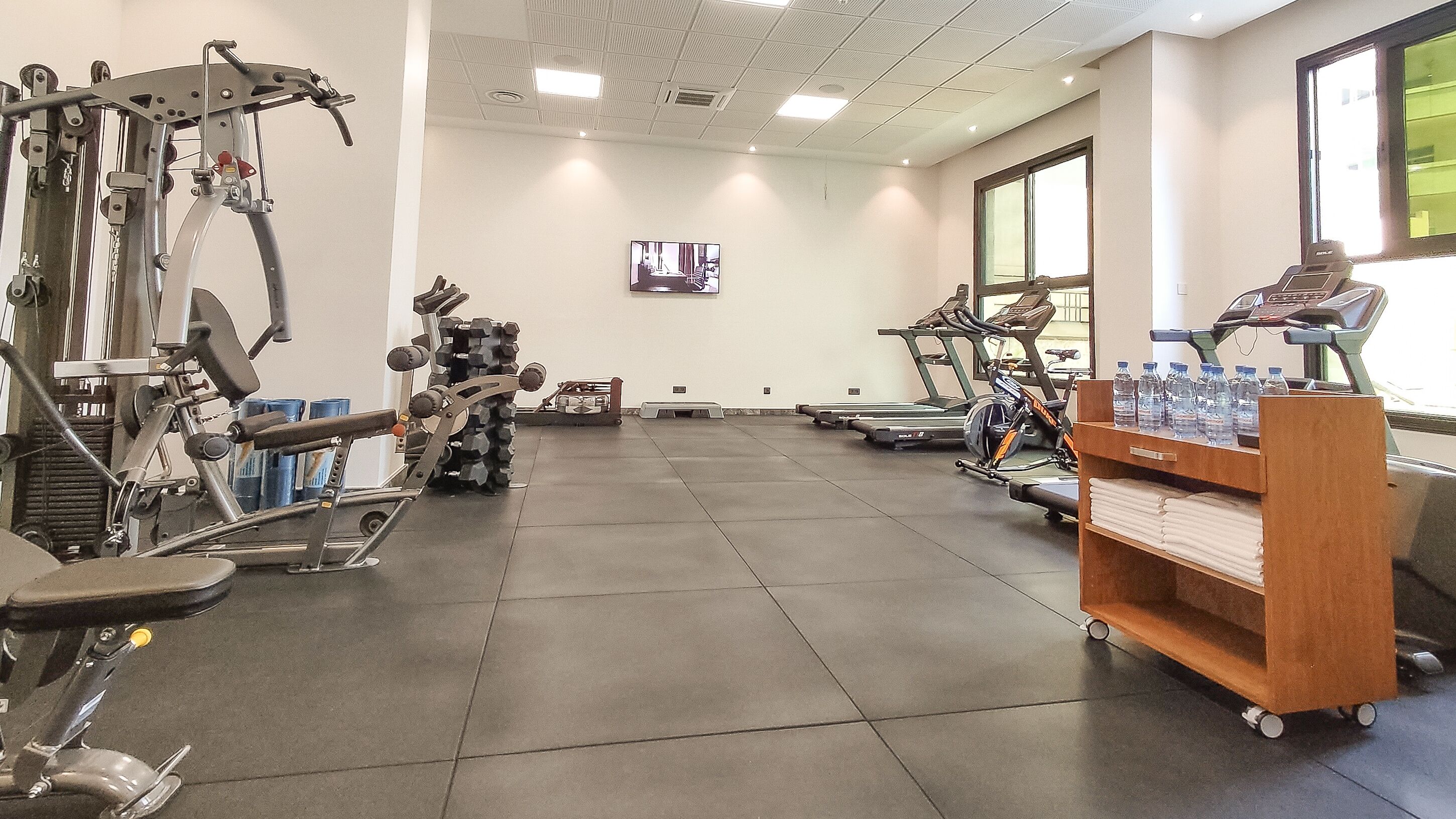 Un gimnasio con diversos equipos de ejercicio, un televisor en la pared y un dispensador de agua.