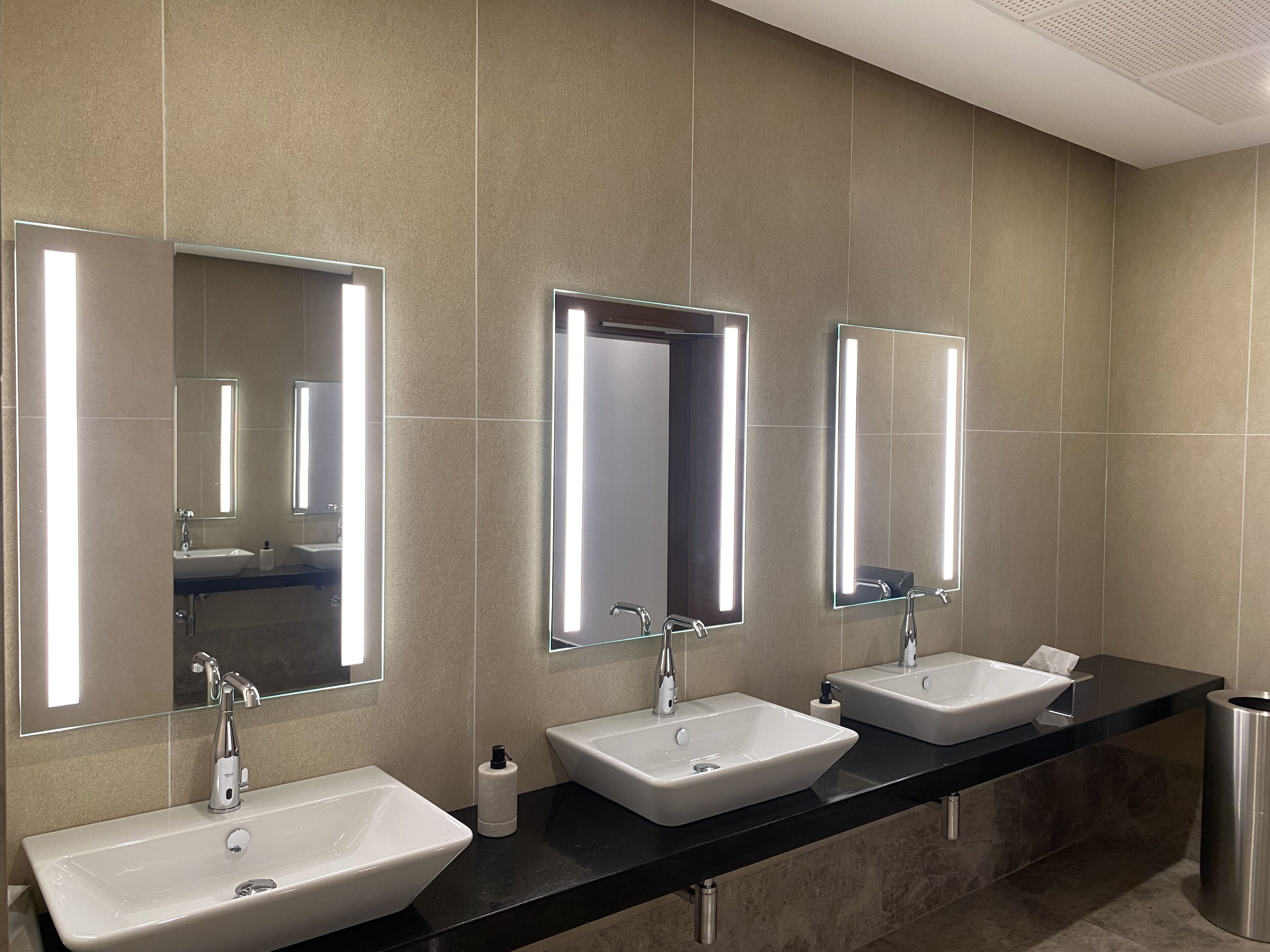 A modern bathroom with three sinks, each with a mirror above.