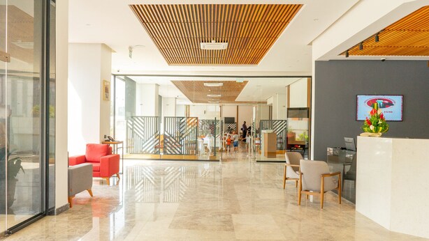 Un moderno vestíbulo de hotel con mostrador de recepción, zona de estar y puertas de vidrio que dan a otras áreas.