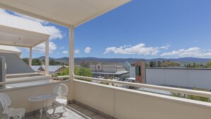 A balcony with a table and chairs, overlooking a town with buildings and mountains in the distance. - Razorback 1/1 Gippsland St (Jindabyne)
