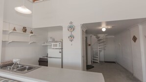 A modern kitchen with white appliances, a built-in oven, and a stainless steel sink. There are white shelves above the counter and a spiral staircase leading to another level. - Razorback 1/1 Gippsland St (Jindabyne)