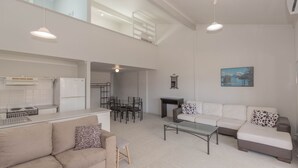 Un vaste espace de vie comprenant un canapé, une table basse en verre et une table à manger avec des chaises. Il y a également un coin cuisine équipé d’un réfrigérateur et d’une cuisinière.
