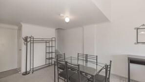Um quarto com uma mesa e cadeiras de vidro, uma estrutura de metal com ganchos, uma lareira e uma luminária no teto.