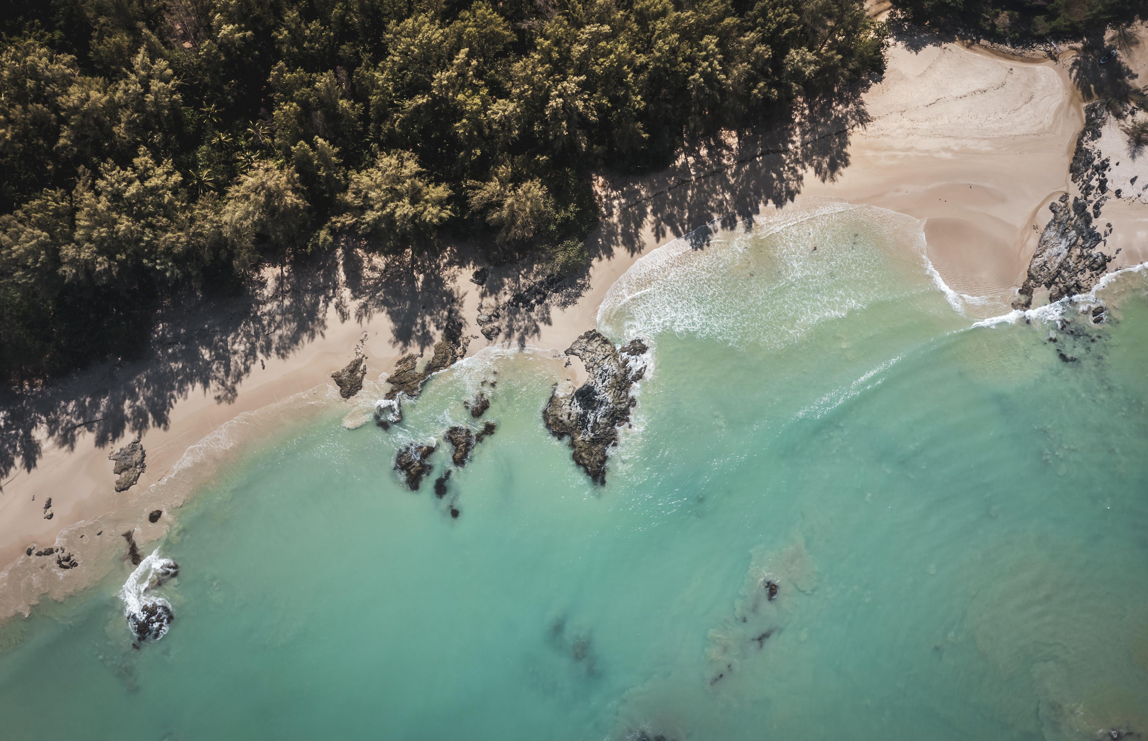 An aerial view of a coastal area with clear turquoise waters, sandy beach, and dense forest.