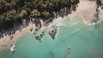 Eine Luftaufnahme einer Küstenregion mit klarem türkisblauem Wasser, Sandstrand und dichtem Wald.
