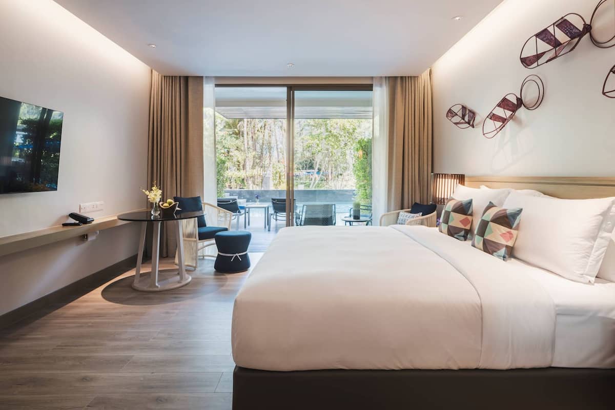 Una habitación de hotel moderna con una cama grande, un escritorio y un balcón con mobiliario de exterior.