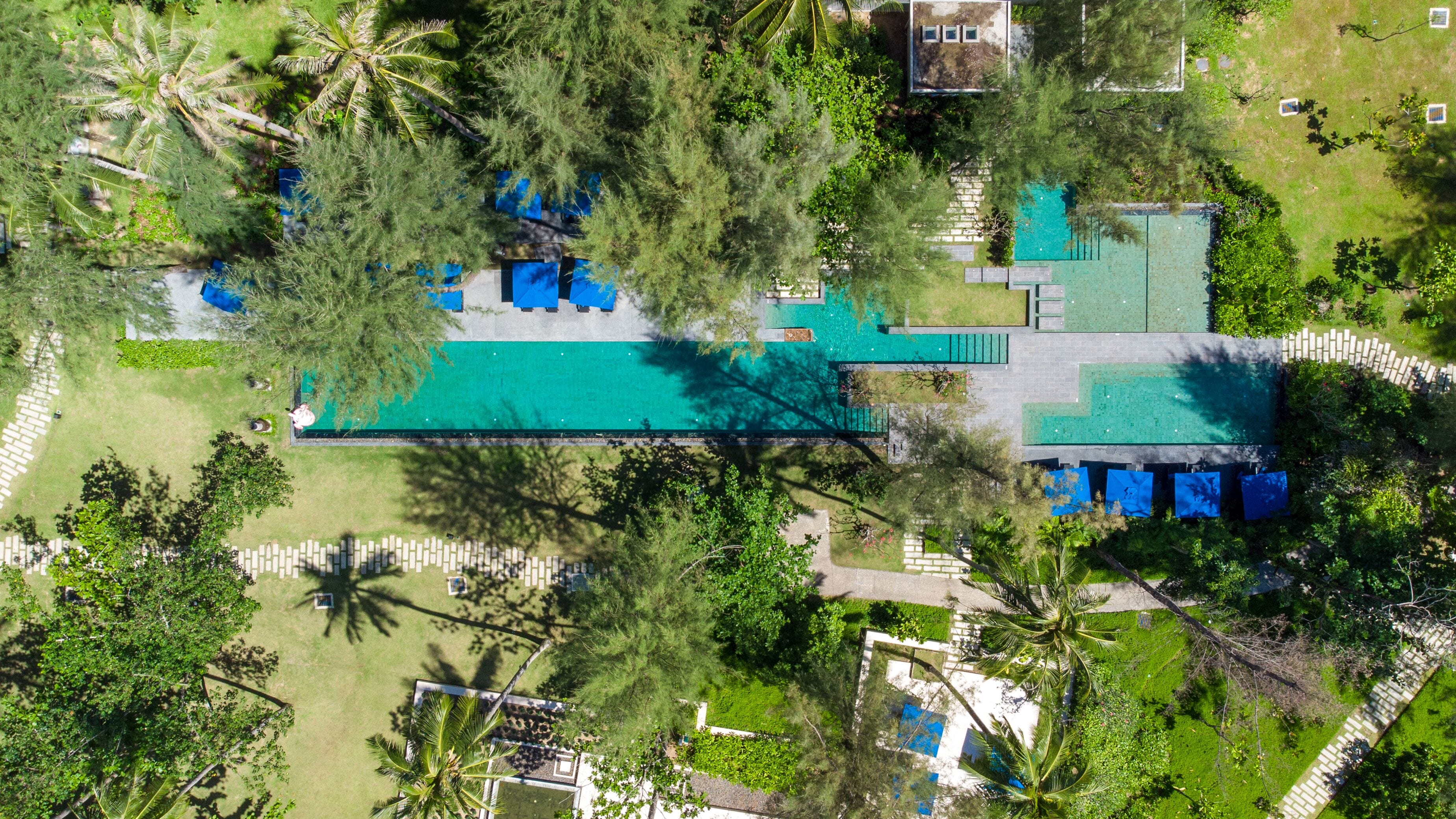 Vista aerea di un resort con una grande piscina, numerose camere e vegetazione rigogliosa.
