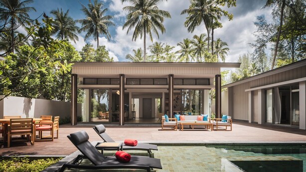 A modern outdoor pool area with lounge chairs and a covered seating area, surrounded by tall palm trees.