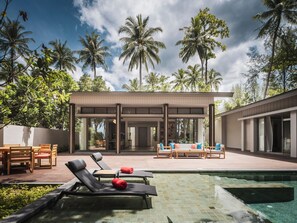 A modern outdoor pool area with lounge chairs and a covered seating area, surrounded by tall palm trees.