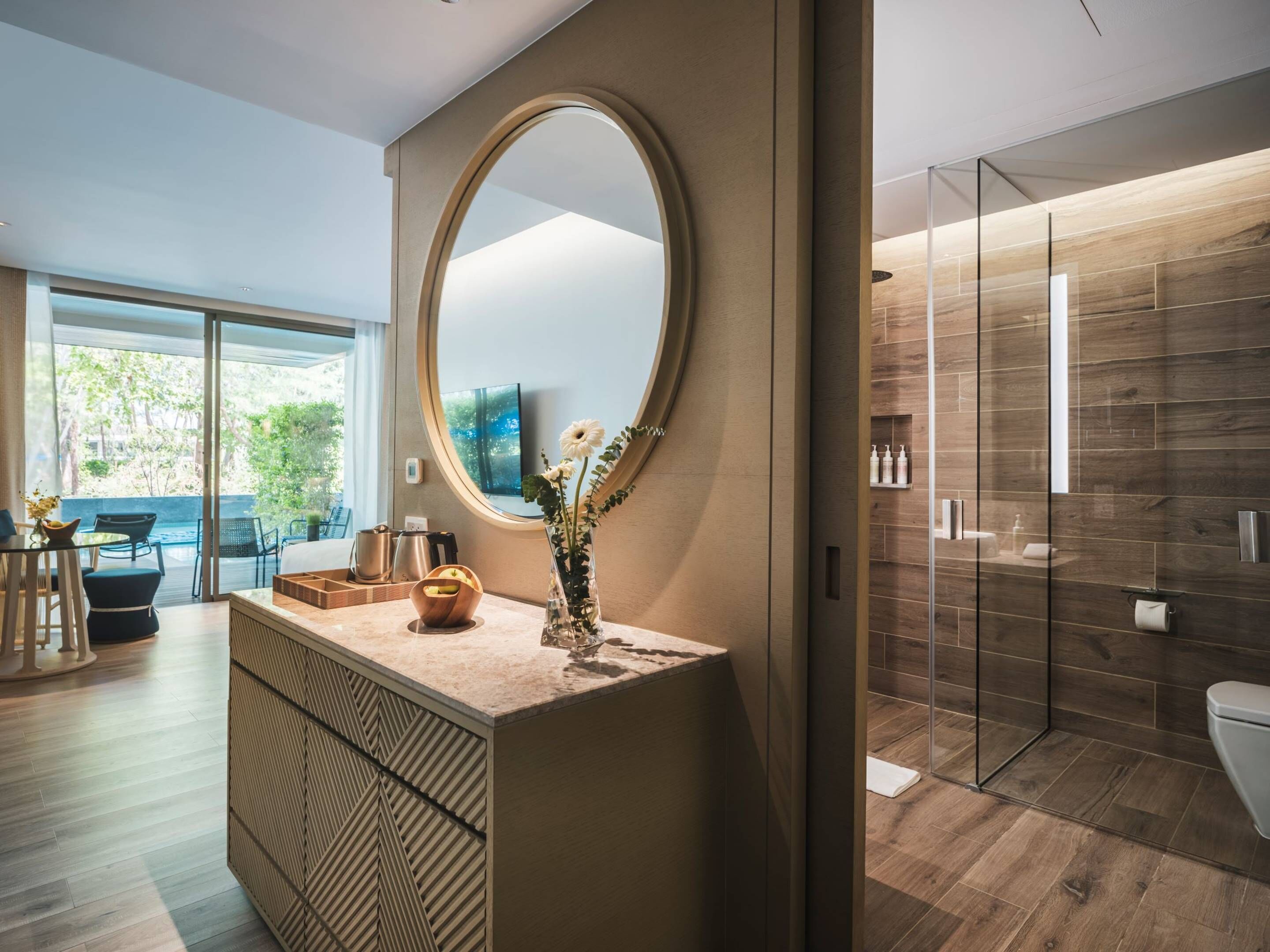 A modern bathroom with a large mirror, wooden flooring, and a glass shower enclosure.
