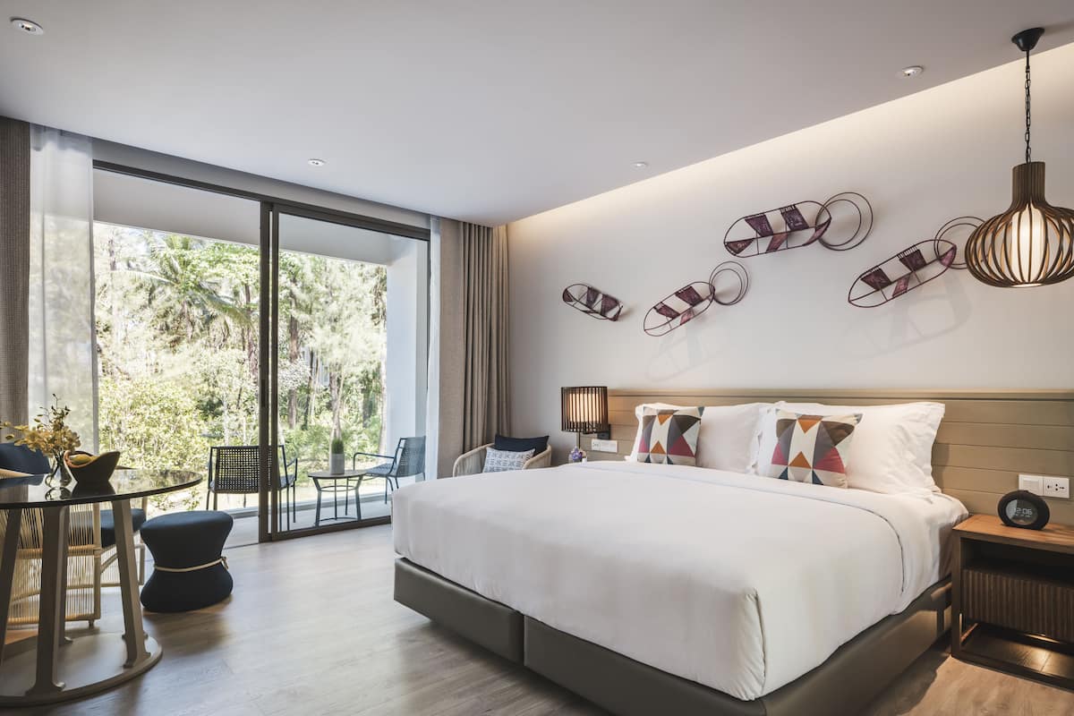 Un dormitorio moderno con una cama grande, una mesa de comedor y sillas, un amplio ventanal con vistas a zonas verdes y decoración en la pared.