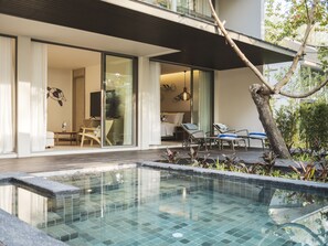 Un espace piscine extérieur moderne, doté d’une structure en verre, d’une terrasse en bois et d’un coin salon avec des chaises et une table.