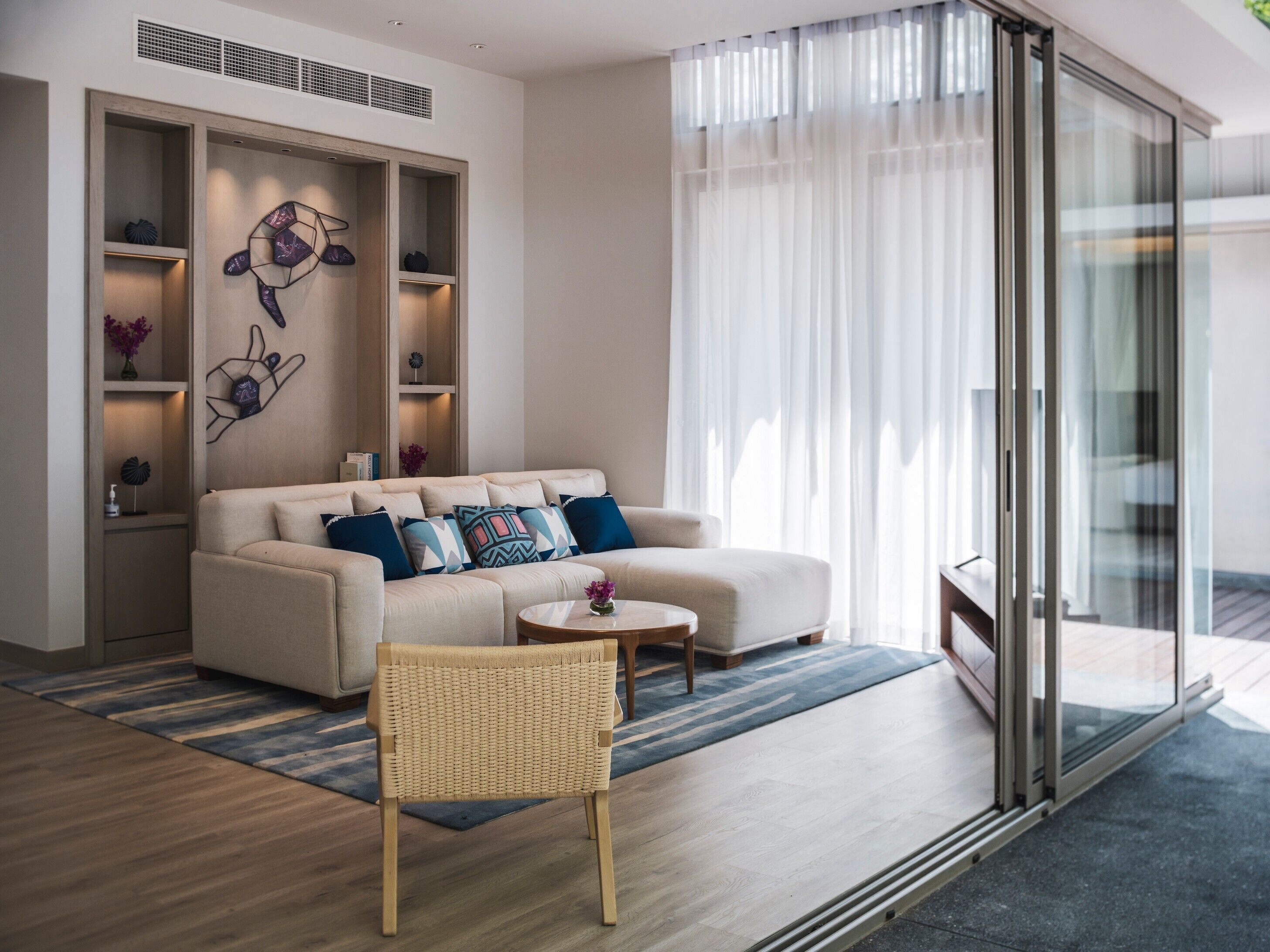 A modern living room with a sofa, a wicker chair, a coffee table, and a glass door leading outside.