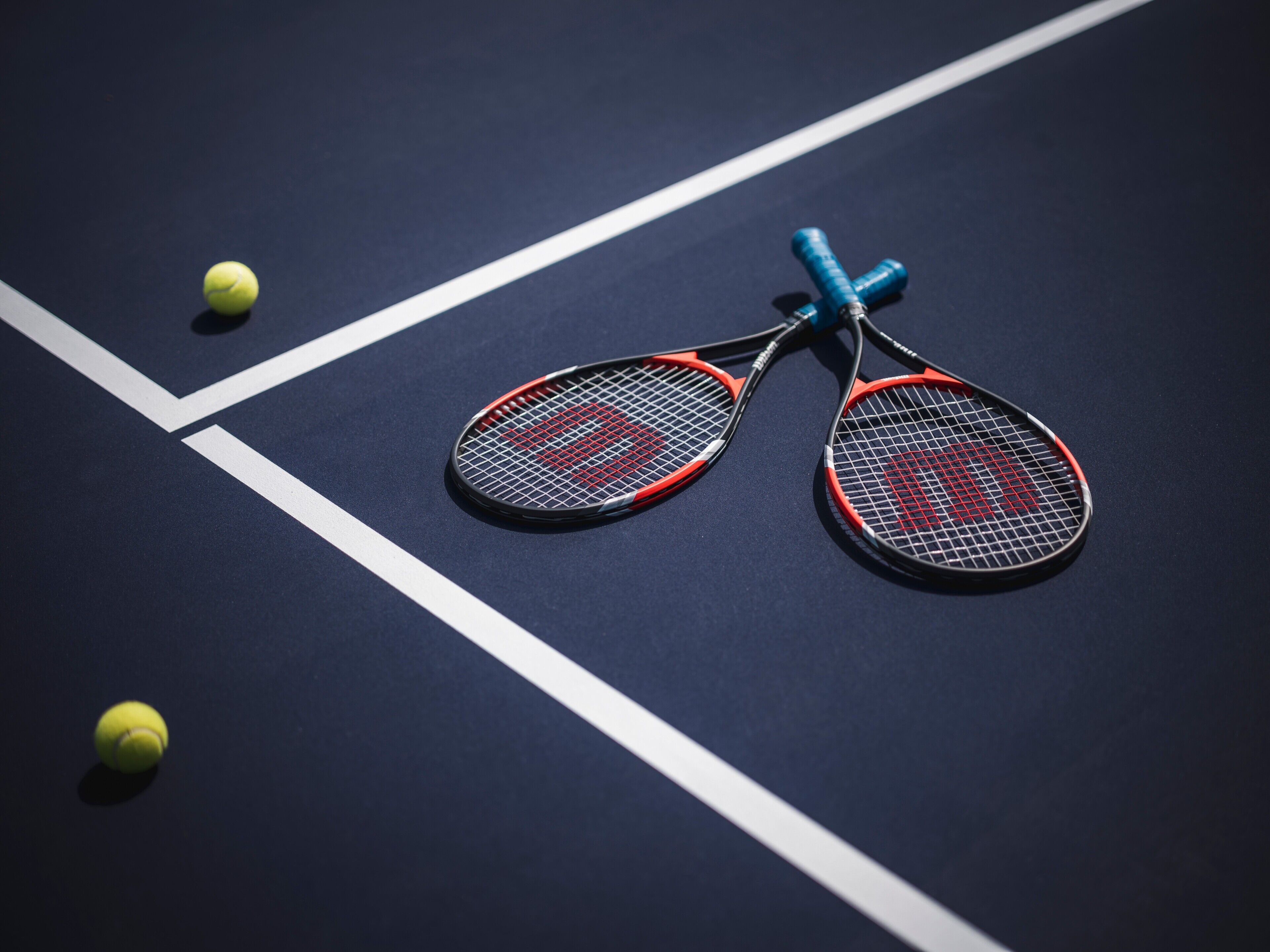 A tennis court with two tennis rackets and two tennis balls.