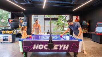 A table hockey game with a "HockeyH" logo, surrounded by arcade games and a large window with a view of trees.