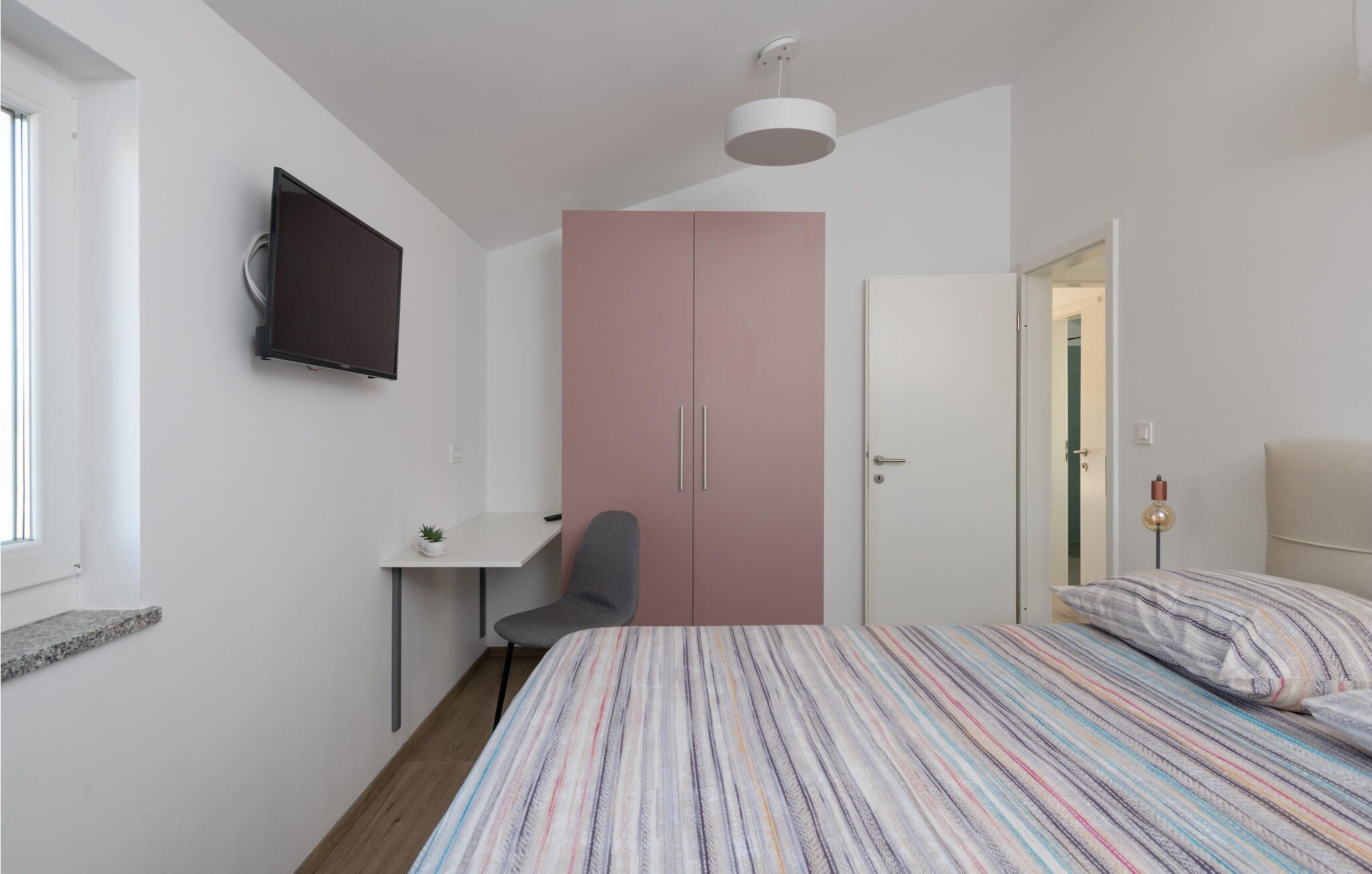 Ein Schlafzimmer mit einem Bett, einem Schreibtisch, einem Stuhl, einem Kleiderschrank und einem Fernseher.