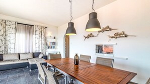 A modern dining area with a wooden table and chairs, a sofa, and decorative wall art. - Cap Ras 01 – Apartment with terrace and sea views (Llança)