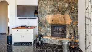 A modern living room with a stone fireplace, a flat-screen TV, and a wooden cabinet. - Cap Ras 01 – Apartment with terrace and sea views (Llança)