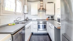 A modern kitchen with white cabinets, stainless steel appliances, and a black tiled floor. - Cap Ras 01 – Apartment with terrace and sea views (Llança)