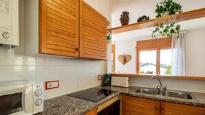 A kitchen with wooden cabinets, a granite countertop, a microwave, a toaster, and a sink. - Cap Ras 04 Comfortable apartment close to the sea (Llança)