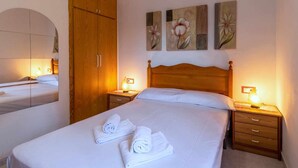 A hotel room with a large bed, two bedside tables, a wooden wardrobe, and three wall-mounted paintings. - Cap Ras 04 Comfortable apartment close to the sea (Llança)