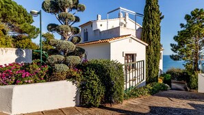 A coastal house with a white facade, a tiled roof, and a small balcony.