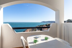A balcony with a view of the sea, a table with two green cups, and a book.