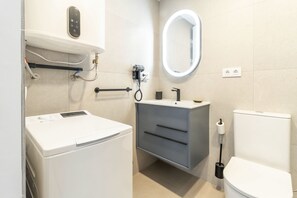 Un baño pequeño con lavadora, lavamanos con espejo e inodoro.