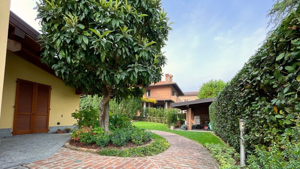 Un vialetto in mattoni conduce a una casa con una porta di legno e un portico coperto.