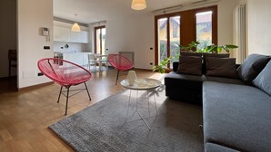 Un soggiorno moderno con un divano grigio, poltrone rosse, un tavolino da caffè e vista sulla cucina e sul balcone.