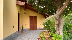 Un edificio con facciata gialla, una porta in legno e un'area d'ingresso coperta con piante in vaso e un albero.
