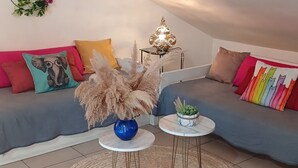 Un salon moderne avec un canapé gris, des coussins colorés, une petite table ronde surmontée d’un vase bleu et un élément décoratif mural.